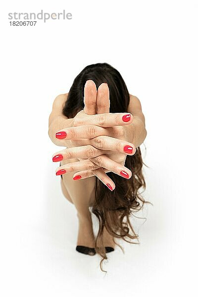 Hockendes Mädchen mit nach vorne gezogenen Händen und gekreuzten Fingern (Foto mit geringer Tiefenschärfe)