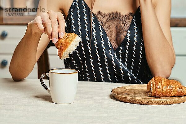 Schöne gemischtrassige Frau isst morgens in der Küche ein frisches Croissant