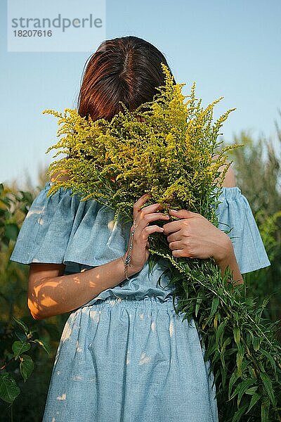 Hübsches Mädchen versteckt Gesicht in Feld mit Blumen