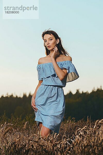 Schönes Mädchen im Weizenfeld bei Sonnenuntergang. Mädchen im lässigen blauen Kleid genießt den sonnigen Abend