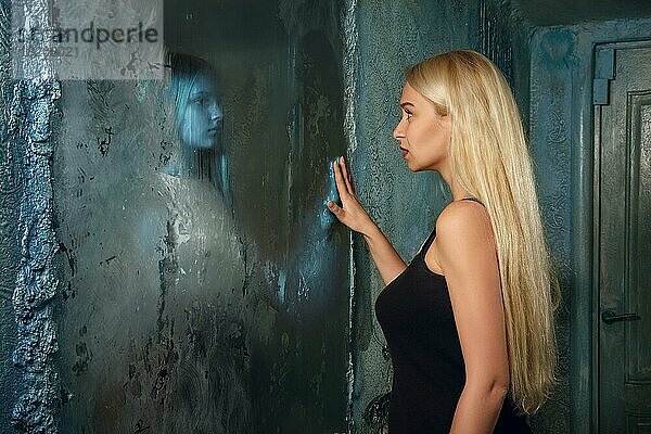 Verängstigte junge Frau schaut in den Spiegel und sieht in der Reflexion ein Geistermädchen
