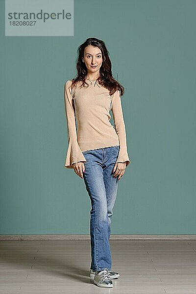 Ganzkörperporträt einer trendigen jungen Frau in beigem Jersey-Longsleeve und geraden blauen Jeans