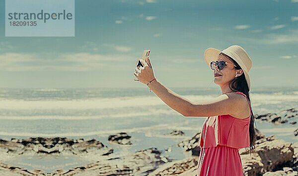 Junge Frau im Urlaub macht Fotos am Strand  Lächelndes Mädchen mit Hut macht Fotos am Strand. Strandurlaub Konzept. Mädchen mit Hut am Strand nehmen ein Selfie