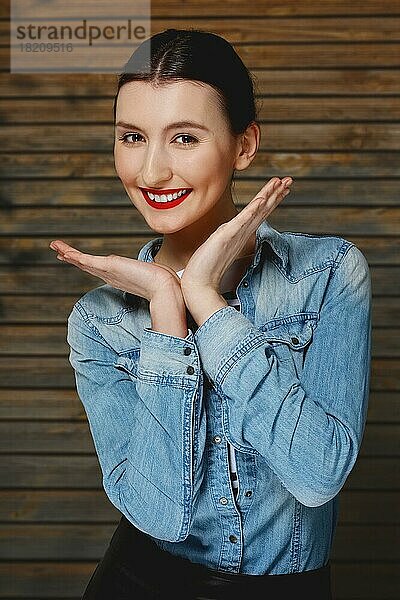 Hübsche Mode-Modell in Jeans-Shirt mit tan Make-up und roten Lippen Matte auf hölzernen Hintergrund