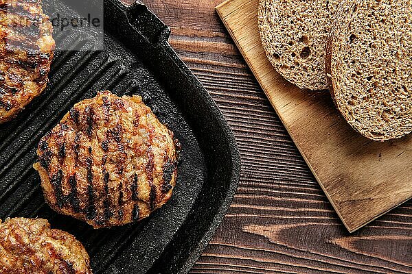 Draufsicht auf eine gusseiserne Grillpfanne mit Rinderkoteletts und frisch gebackenem Schwarzbrot