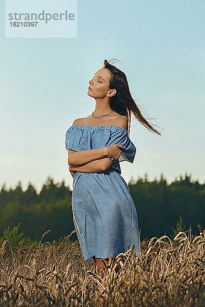 Schönes Mädchen im Weizenfeld bei Sonnenuntergang. Mädchen im lässigen blauen Kleid genießt den sonnigen Abend