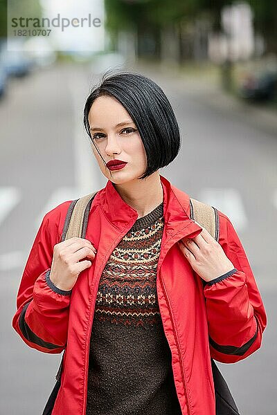 Closeup Porträt von niedlichen nachdenklich Mädchen in roter Jacke und Rucksack auf der Straße