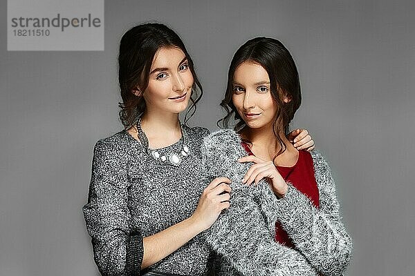 Zwei junge Schwestern in warmen Wollpullovern umarmen sich gegenseitig