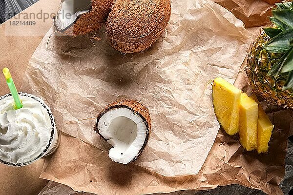 Draufsicht auf das ungefaltete Papier auf dem Tisch mit gespaltener Kokosnuss  Ananas in Scheiben und cremigem Milchcocktail