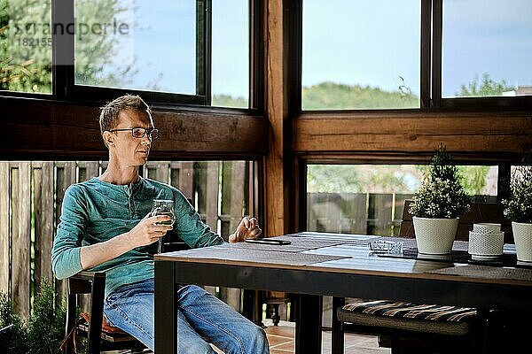 Ein Mann mittleren Alters ruht sich mit einem Glas Wein auf der Veranda aus und stellt einen eingehenden Anruf zurück