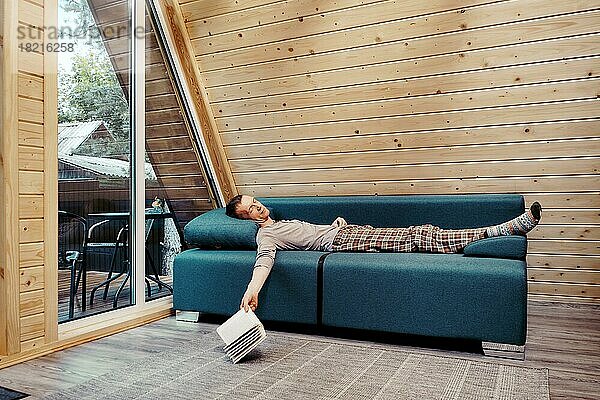 Ein Mann mittleren Alters schläft friedlich auf dem Sofa in seinem Landhaus. Er ließ das Buch auf den Boden fallen