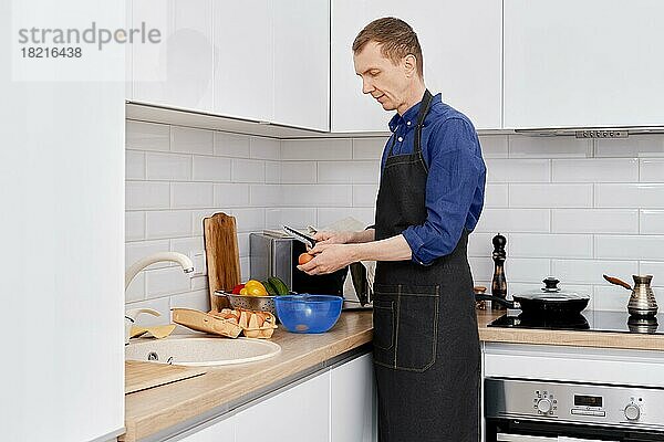Ein Mann mittleren Alters schlägt ein Ei in einer Schüssel auf  um ein Omelett zu machen