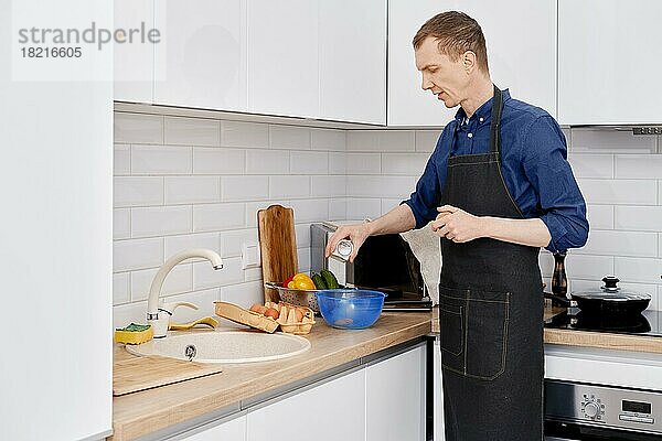 Mann mittleren Alters schüttet Salz in die Küche und macht ein Omelett