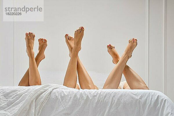 Niedriger Blickwinkel auf drei Paare gekreuzter Frauenbeine im Bett
