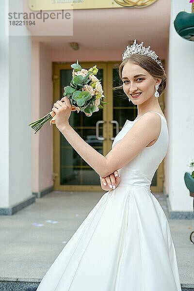 Porträt der schönen Braut mit Krönchen hält Blumenstrauß in den Händen im Freien