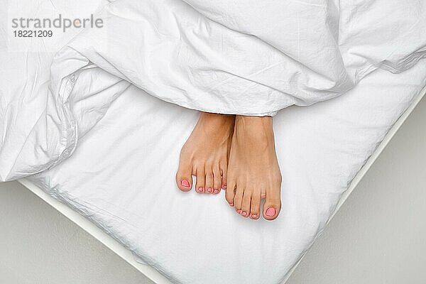 Draufsicht auf weibliche Zehen  die unter der Bettdecke hervorschauen