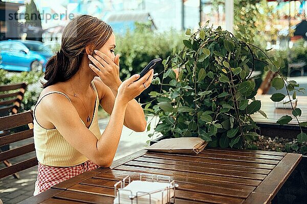 Hübsche Frau benutzt den Bildschirm ihres Smartphones als Spiegel im Freien