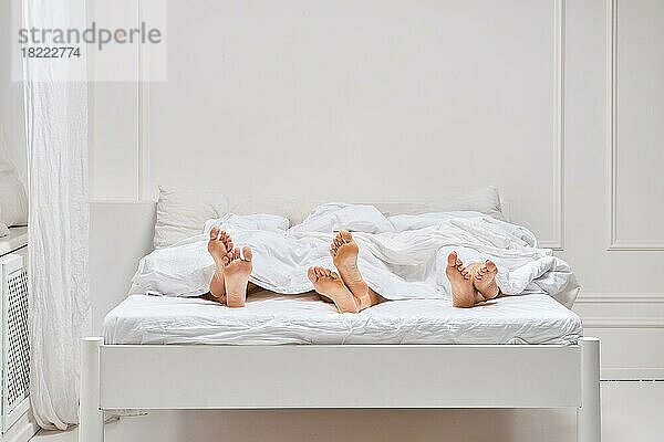 Drei Paar Frauenbeine  die unter der Decke hervorlugen. Konzept für einen faulen Morgen
