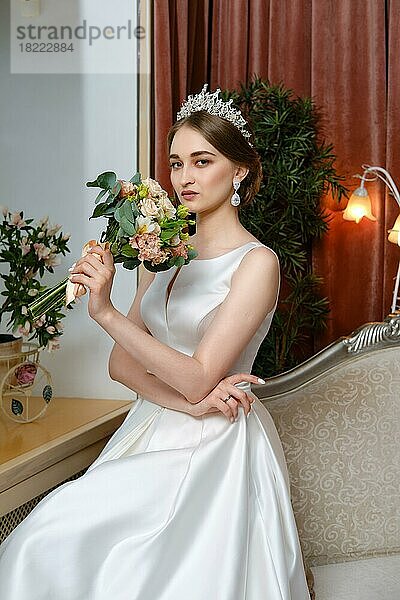 Schöne Braut in lond Kleid sitzt auf der Couch am Fenster