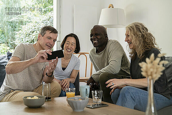Älterer Mann teilt Bilder auf dem Smartphone mit Freunden  während er auf dem Sofa sitzt