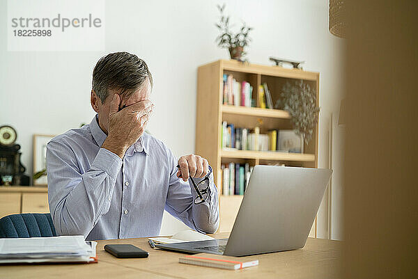 Gestresster älterer Geschäftsmann mit der Hand im Gesicht beim Homeoffice