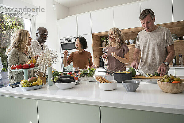Verschiedene Freunde mittleren Alters amüsieren sich in der Küche beim Zubereiten des Abendessens