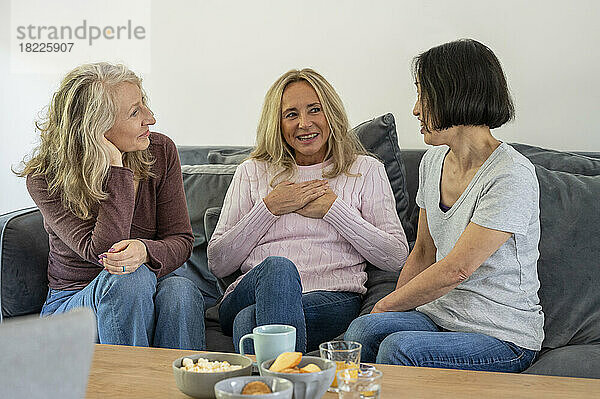 Drei ältere Freundinnen unterhalten sich  während sie zu Hause auf dem Sofa sitzen