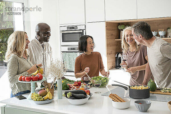 Group of diverse middle-aged friends getting together for dinner chatting in kitchen while cooking