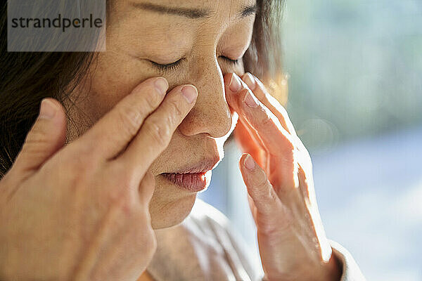 Nahaufnahme einer älteren asiatischen Frau  die ihr Gesicht berührt