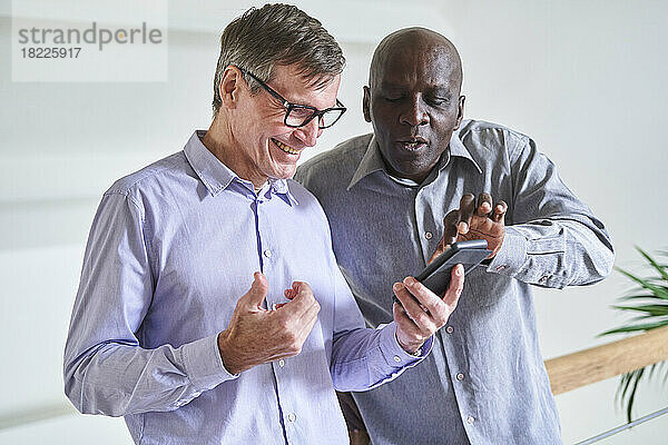 Zwei ältere  vielfältige männliche Freunde schauen sich zu Hause Fotos auf dem Handy an