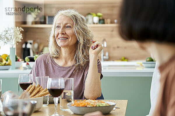 Mid-shot of mature woman sitting at table enjoying meal with friends