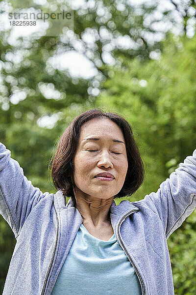 Ältere asiatische Frau hebt die Hände und atmet tief ein