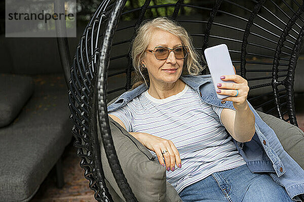 Ältere Frau sitzt in einem bequemen Gartenstuhl und macht ein Selfie