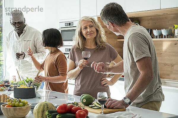 Group of diverse middle aged friends chatting in the kitchen while preparing food