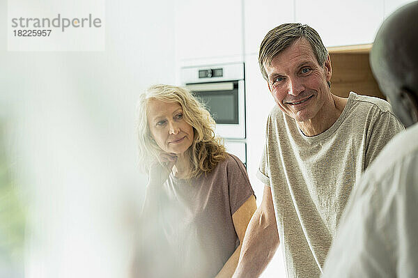 Porträt eines Paares mittleren Alters  das mit Freunden in der Küche plaudert