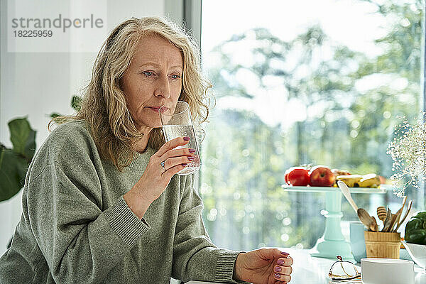 Besorgte ältere Frau trinkt Wasser  während sie an der Theke sitzt