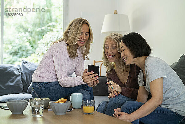 Ältere Frauen schauen sich Videos auf dem Smartphone an  während sie auf dem Sofa sitzen