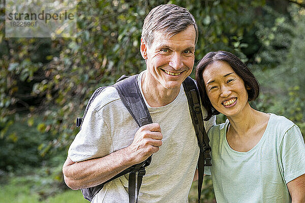 Ein gemischtes Paar mittleren Alters blickt beim Wandern im Wald in die Kamera