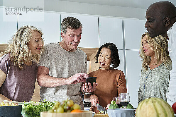 Senior man looking for recipes on smart phone while gathered with friends