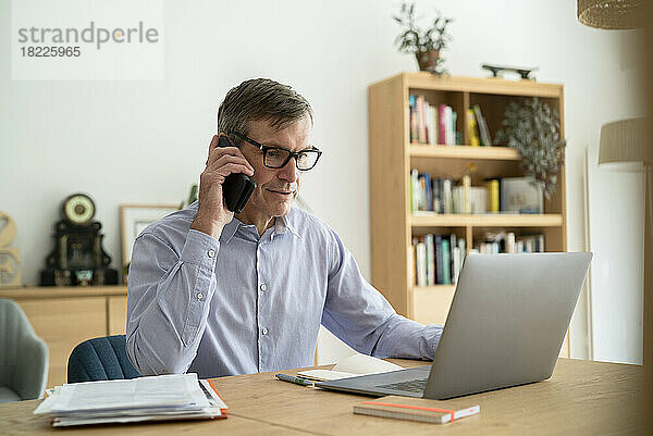 Senior-Geschäftsmann hört im Home-Office Voicemail auf dem Smartphone ab