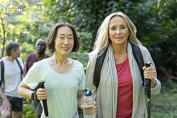 Zwei Frauen mittleren Alters mit Wanderstöcken gehen mit ihren Partnern im Wald spazieren