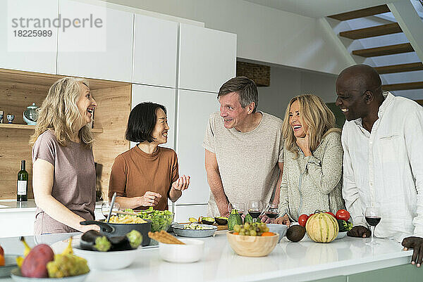 Diverse group of senior friends gathered at kitchen counter while drinking wine