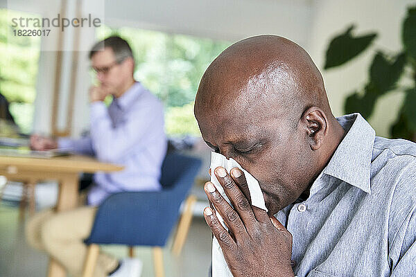 Nahaufnahme eines älteren afroamerikanischen Mannes  dem eine Erkältung die Nase putzt
