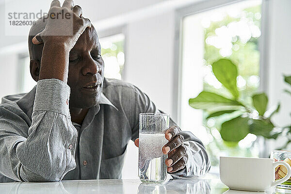 Afroamerikanischer Mann mittleren Alters mit Kopfschmerzen  der seine Medikamente einnimmt