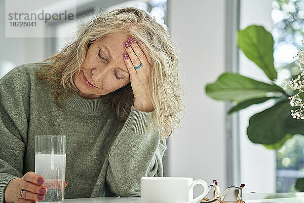Ältere Frau hat Kopfschmerzen  während sie im Esszimmer sitzt