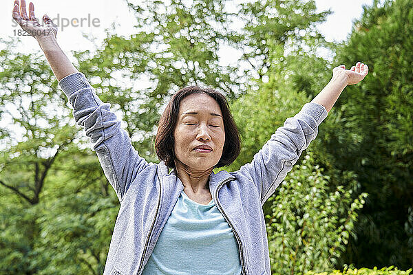 Ältere asiatische Frau streckt sich  während sie die Arme hebt