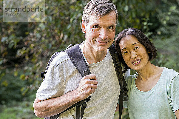 Ein gemischtes Paar mittleren Alters blickt beim Wandern im Wald in die Kamera
