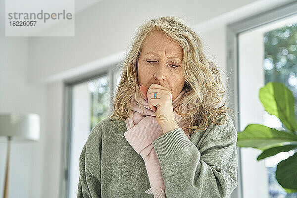 Senior woman sitting indoors while coughing