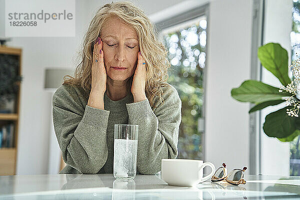 Gestresste ältere Frau berührt ihr Gesicht  während sie Medikamente trinkt