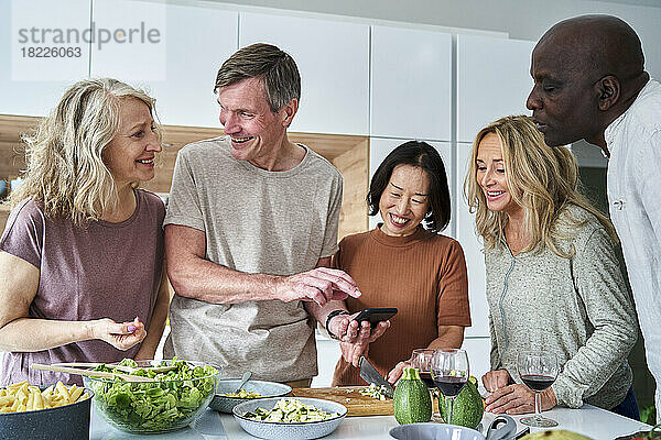 Eine vielfältige Gruppe älterer Freunde versammelte sich in der Küche  während sie ihr Smartphone benutzten